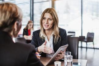 2 people sitting at a table with one holding an ipad